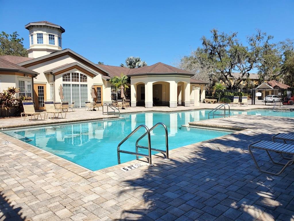 A swimming pool with a metal ladder sits in front of a tan clubhouse building — 8327 PINE RIVER ROAD, TAMPA, FL
