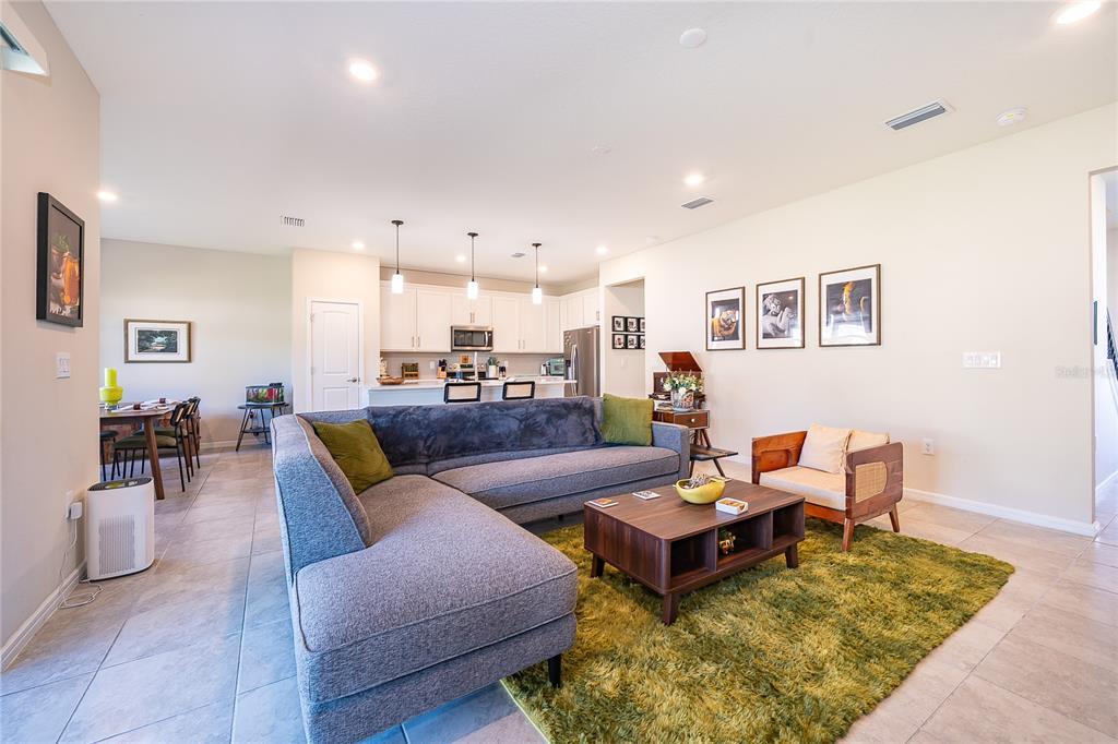 An open-concept kitchen with white cabinets and a breakfast bar overlooks a tiled living area — 17532 SAW PALMETTO AVENUE, CLERMONT, FL