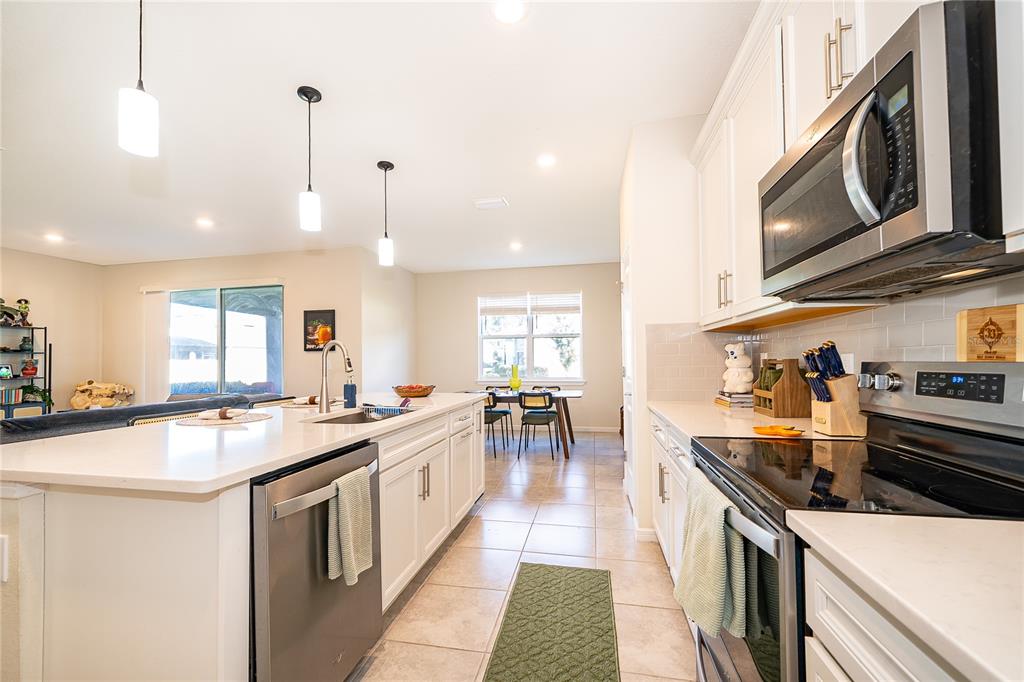 A modern kitchen features white cabinetry, a central island, stainless steel appliances, and tile flooring — 17532 SAW PALMETTO AVENUE, CLERMONT, FL