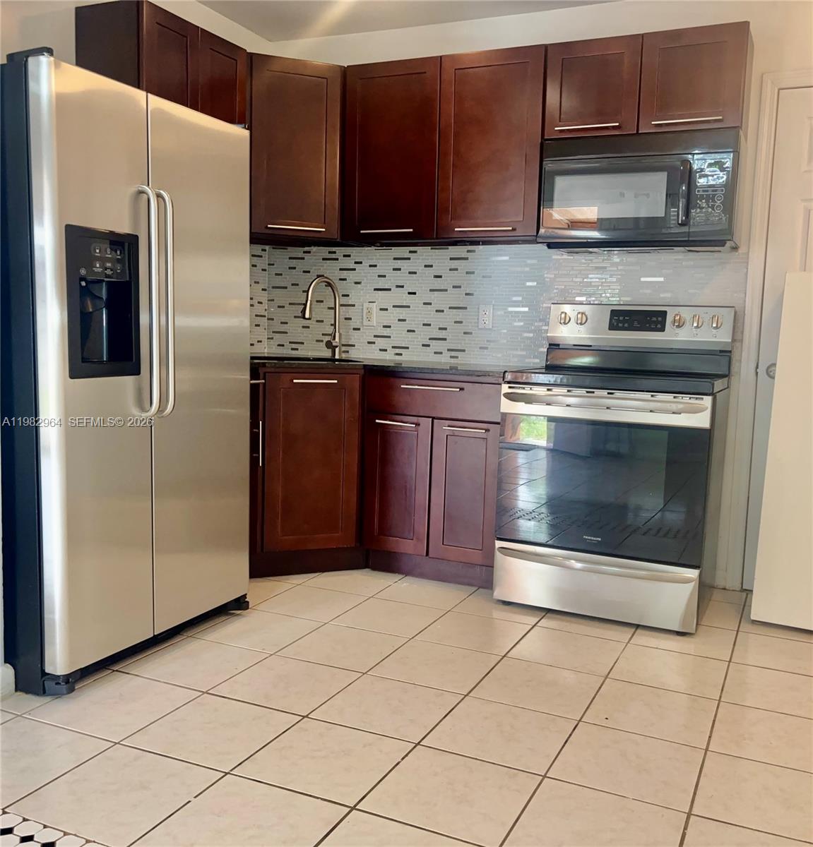 A kitchen features dark wood cabinets, stainless steel appliances, a tiled backsplash, and light flooring — 2016 NE 26th St # 2, Wilton Manors FL 33305, WILTON MANORS, FL