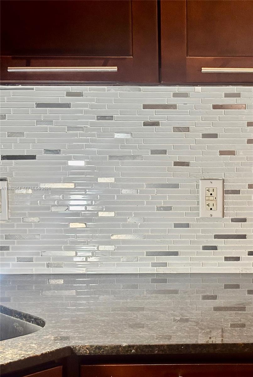 A kitchen backsplash features horizontal glass and metallic tiles above a dark granite countertop — 2016 NE 26th St # 2, Wilton Manors FL 33305, WILTON MANORS, FL