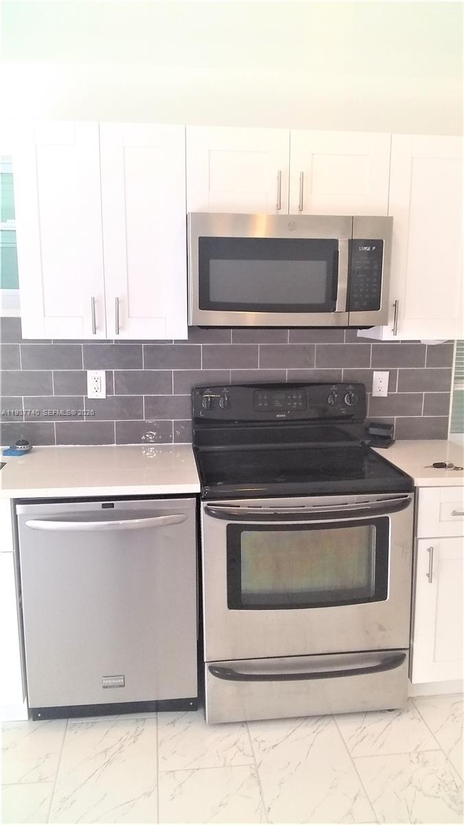 A kitchen features white cabinets, stainless steel appliances, and a gray subway tile backsplash — 710 52nd St, West Palm Beach FL 33407, WEST PALM BEACH, FL