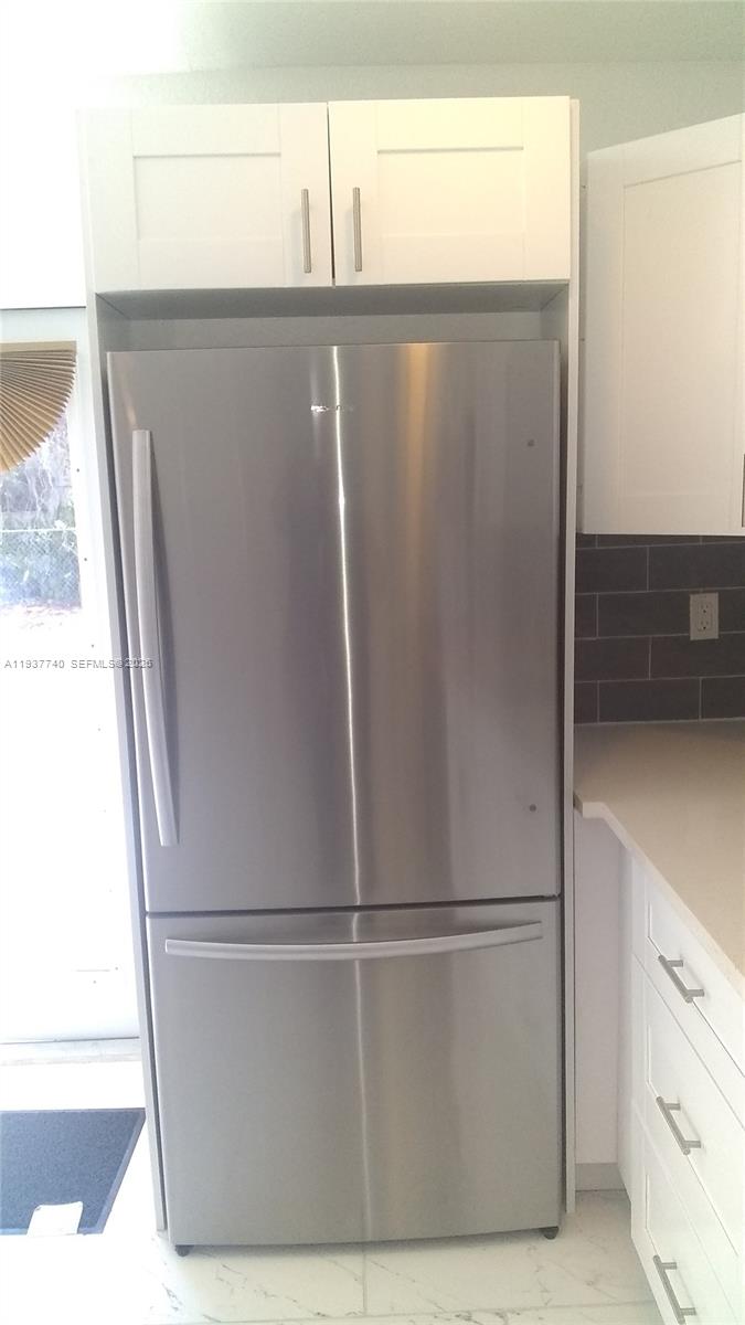 A stainless steel refrigerator is built into a kitchen cabinet unit with white shaker cabinets — 710 52nd St, West Palm Beach FL 33407, WEST PALM BEACH, FL