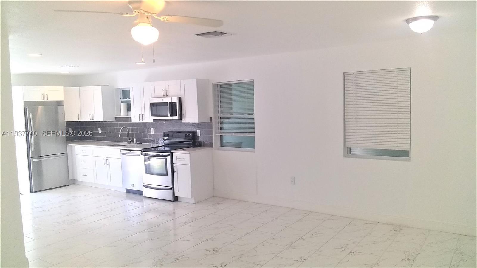A kitchen with white cabinets, stainless steel appliances, and tile flooring opens to a room — 710 52nd St, West Palm Beach FL 33407, WEST PALM BEACH, FL