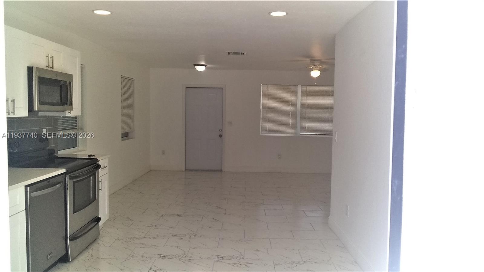 A kitchen with white cabinets and stainless steel appliances opens into a tiled living area — 710 52nd St, West Palm Beach FL 33407, WEST PALM BEACH, FL