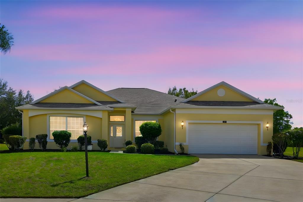 A yellow single-story house with a two-car garage and a paved driveway at sunset — 3810 ST EMMA COURT, LEESBURG, FL