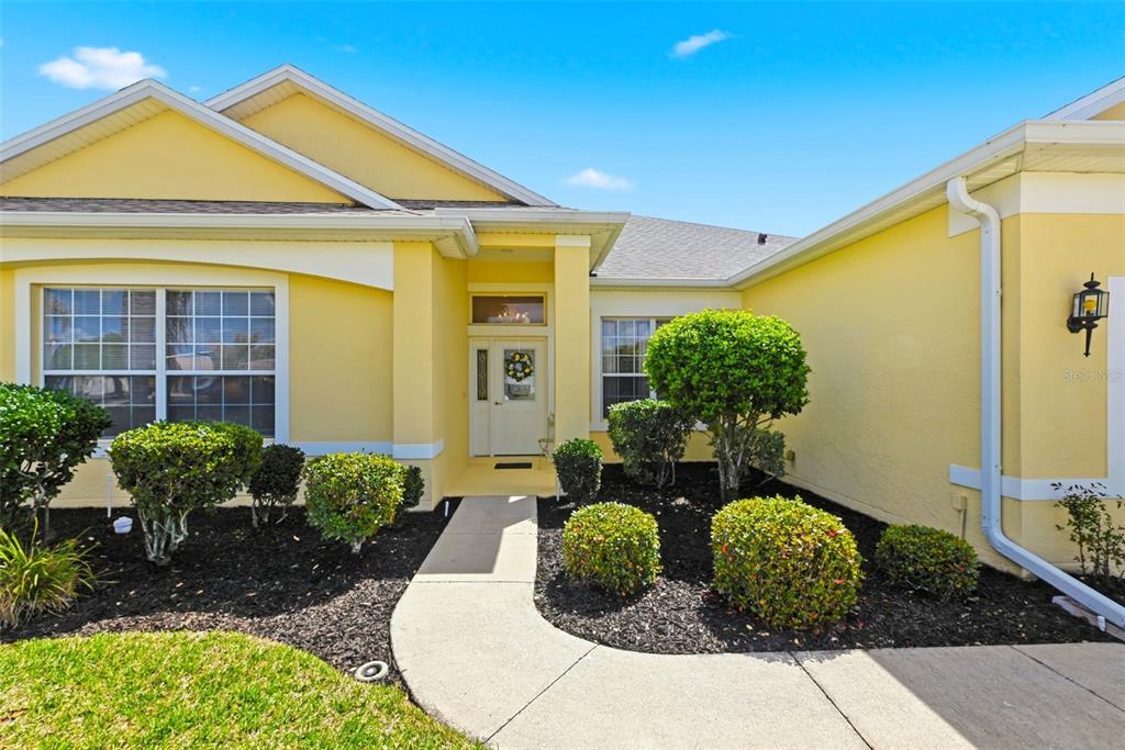 A yellow house exterior features a concrete walkway leading to a white front door — 3810 ST EMMA COURT, LEESBURG, FL