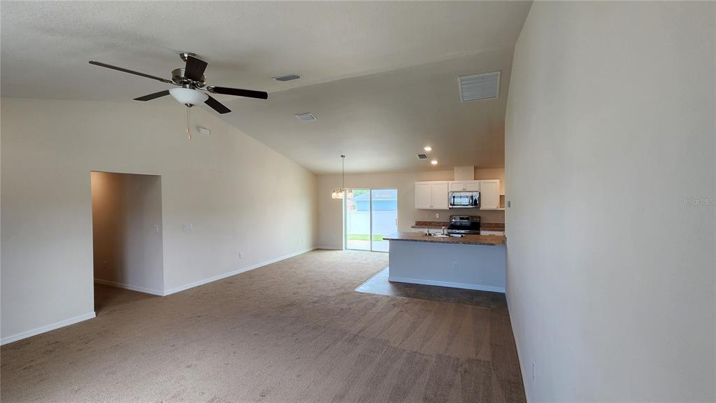 An open-concept living area features carpeted flooring, a vaulted ceiling, and an adjacent kitchen — 680 W MARGUERITA DRIVE, DUNNELLON, FL