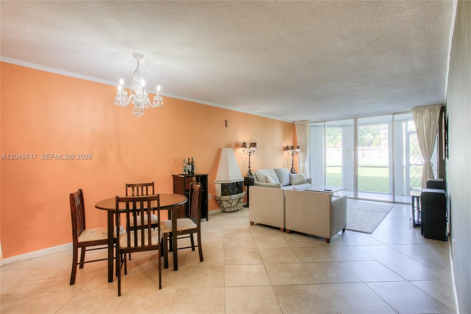 A living and dining area with peach walls, tile floors, and a corner fireplace — 1501 NE 191st St # C106, Miami FL 33179, MIAMI, FL