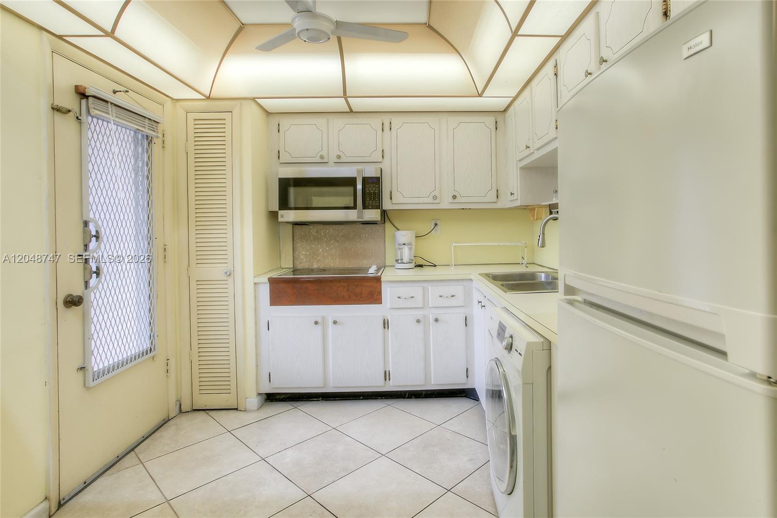 A kitchen features white cabinets, a built-in microwave, a washer, and a tiled floor — 1501 NE 191st St # C106, Miami FL 33179, MIAMI, FL