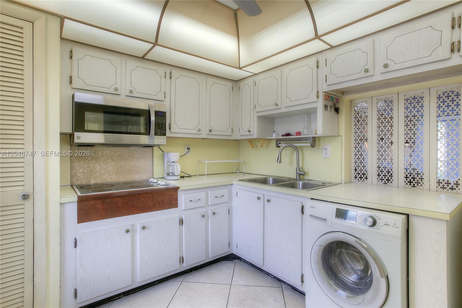 A kitchen features white cabinets, a stainless steel microwave, a sink, and a front-loading washer — 1501 NE 191st St # C106, Miami FL 33179, MIAMI, FL