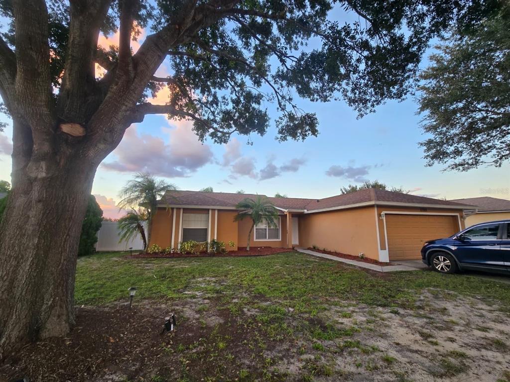 A single-story house with an orange exterior, a two-car garage, and a large front tree — 13303 PINYON DRIVE, CLERMONT, FL