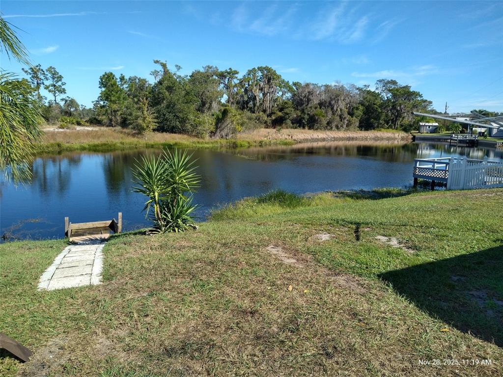 A grassy backyard slopes down to a small pond with a wooden dock and deck — 8454 BREEZE HILL DRIVE, LAKE WALES, FL