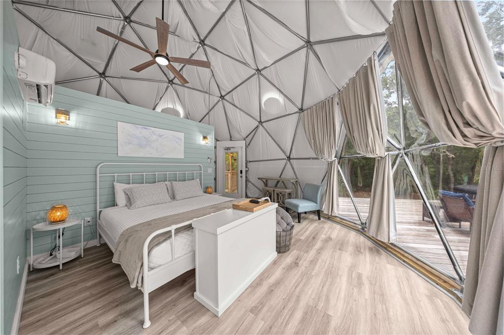 A bedroom inside a geodesic dome features a white bed, light wood flooring, and large windows — 414 S SCHOOL AVENUE, LECANTO, FL