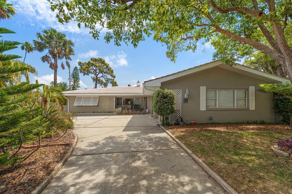 A single-story house with a concrete driveway, tan exterior, and a large tree in front — 109 PONCE DE LEON BOULEVARD, BELLEAIR, FL