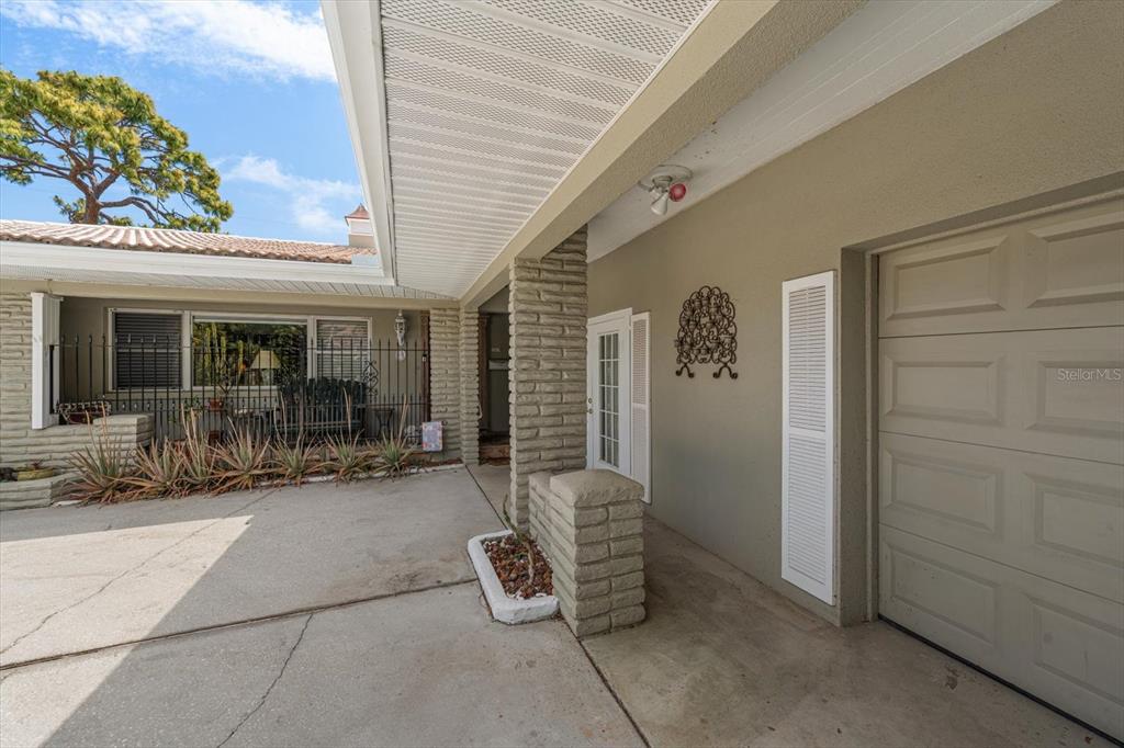 A concrete driveway leads to a covered entryway with a brick pillar and garage door — 109 PONCE DE LEON BOULEVARD, BELLEAIR, FL