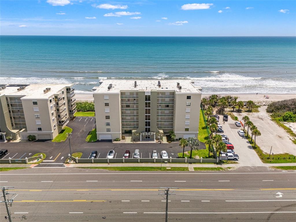 An aerial view shows two beachfront apartment buildings with parking lots along a coastal road — 407 HIGHWAY A1A UNIT 443, SATELLITE BEACH, FL