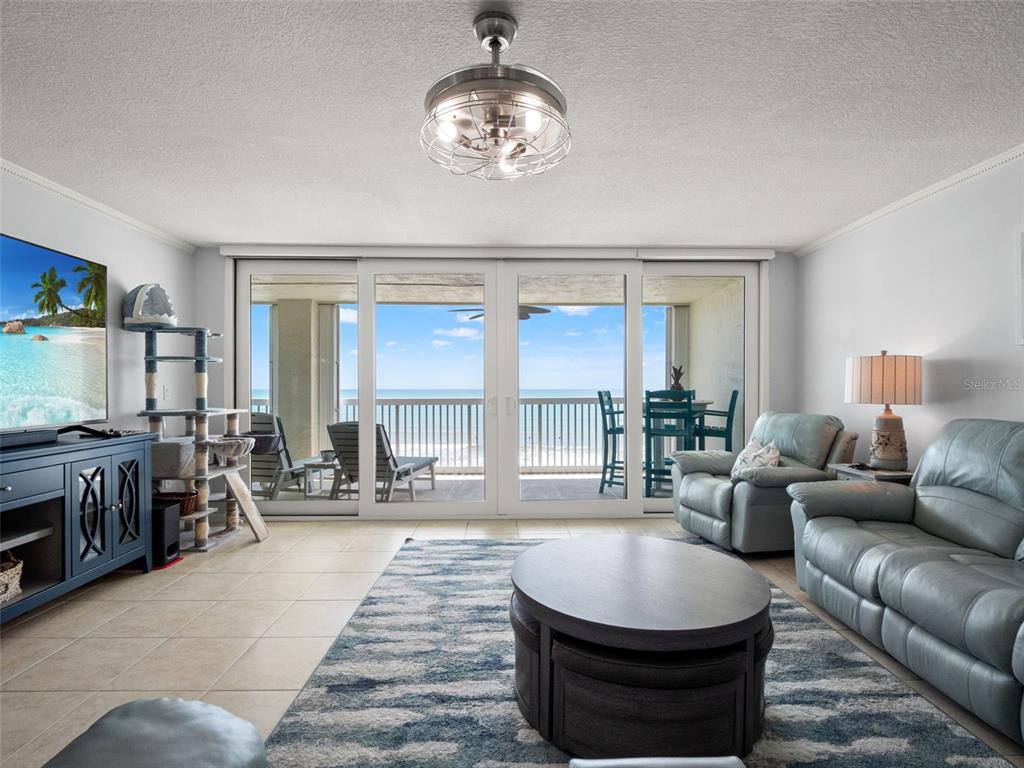 A living room features a blue media console, leather seating, and a balcony overlooking the ocean — 407 HIGHWAY A1A UNIT 443, SATELLITE BEACH, FL