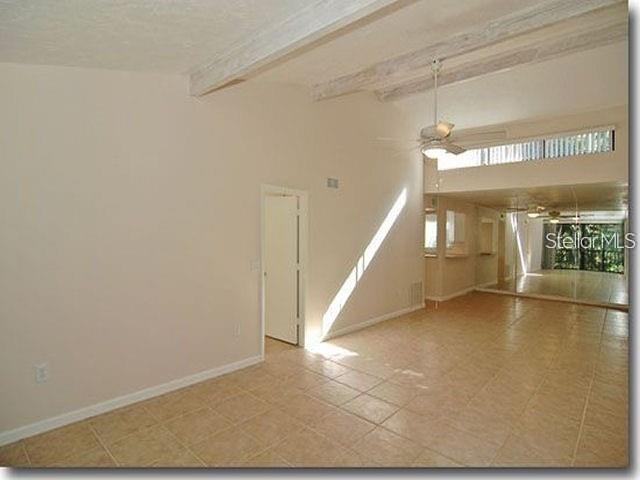 A spacious living room with vaulted ceilings, exposed beams, tile flooring, and a ceiling fan — 1508 PELICAN COVE ROAD UNIT 238, SARASOTA, FL