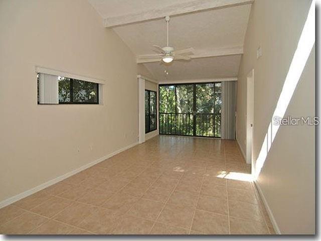 An empty living room with beige tile floors, a vaulted ceiling, and a large sliding door — 1508 PELICAN COVE ROAD UNIT 238, SARASOTA, FL