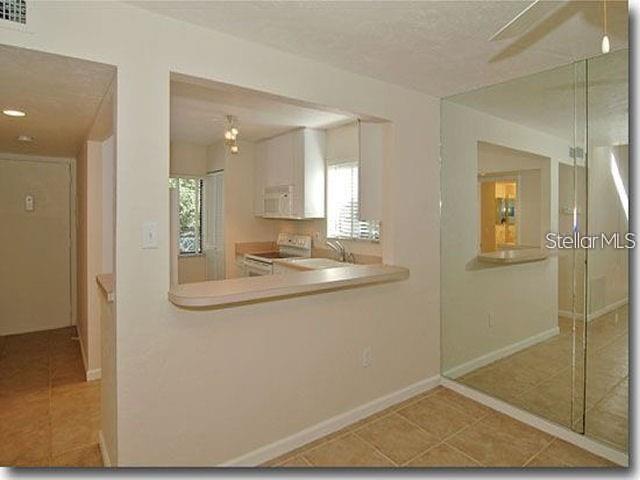A kitchen with white cabinets is viewed through a pass-through window from a tiled room — 1508 PELICAN COVE ROAD UNIT 238, SARASOTA, FL