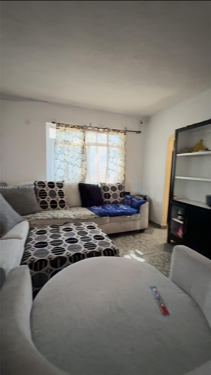 A living room features a white sofa with patterned pillows, a matching ottoman, and shelving — 110 NW 52nd St, Miami FL 33127, MIAMI, FL