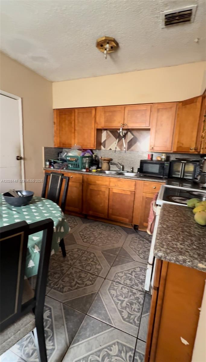 A kitchen features wooden cabinets, a patterned tile floor, and a small dining table — 110 NW 52nd St, Miami FL 33127, MIAMI, FL