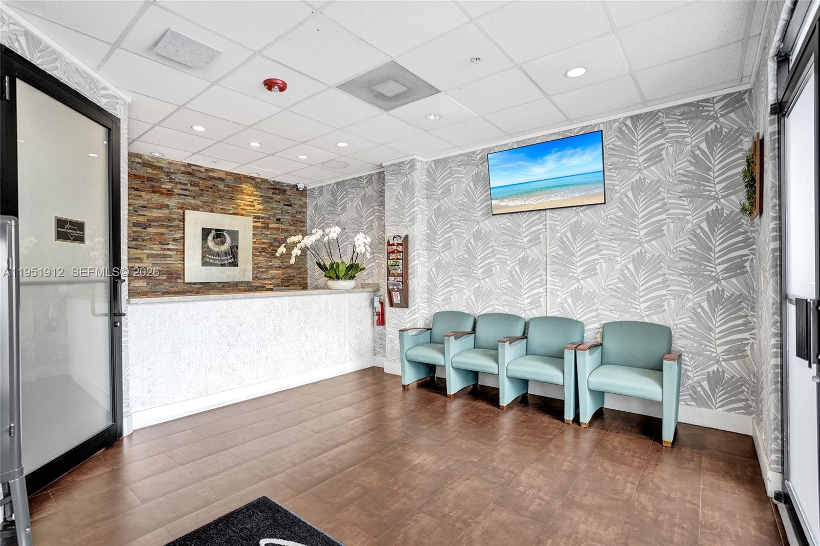 A waiting room features a stone reception desk, teal chairs, and palm-patterned wallpaper — 7374 SW 93rd Ave # B, Miami FL 33173, MIAMI, FL