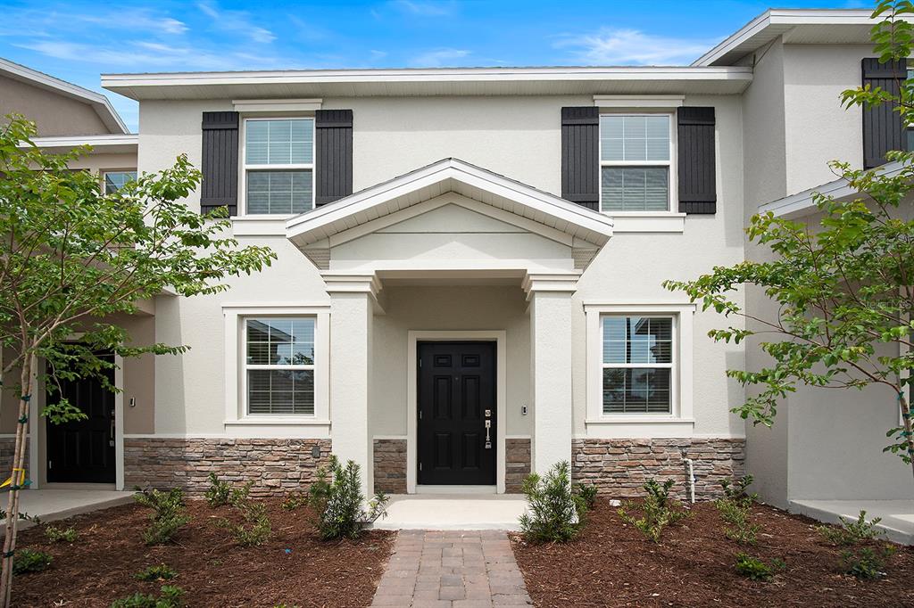 A two-story townhouse exterior with a stone veneer base, black shutters, and a covered entryway — 5643 QUIET PALM LOOP, ST CLOUD, FL