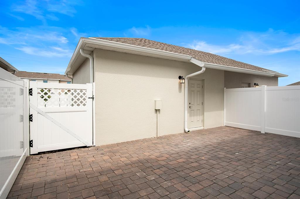 A paved patio area sits beside a beige building with a white door and fence — 5643 QUIET PALM LOOP, ST CLOUD, FL