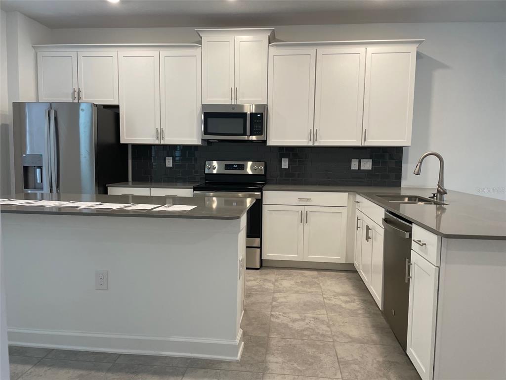 A modern kitchen features white cabinets, stainless steel appliances, gray countertops, and dark subway tile — 5643 QUIET PALM LOOP, ST CLOUD, FL