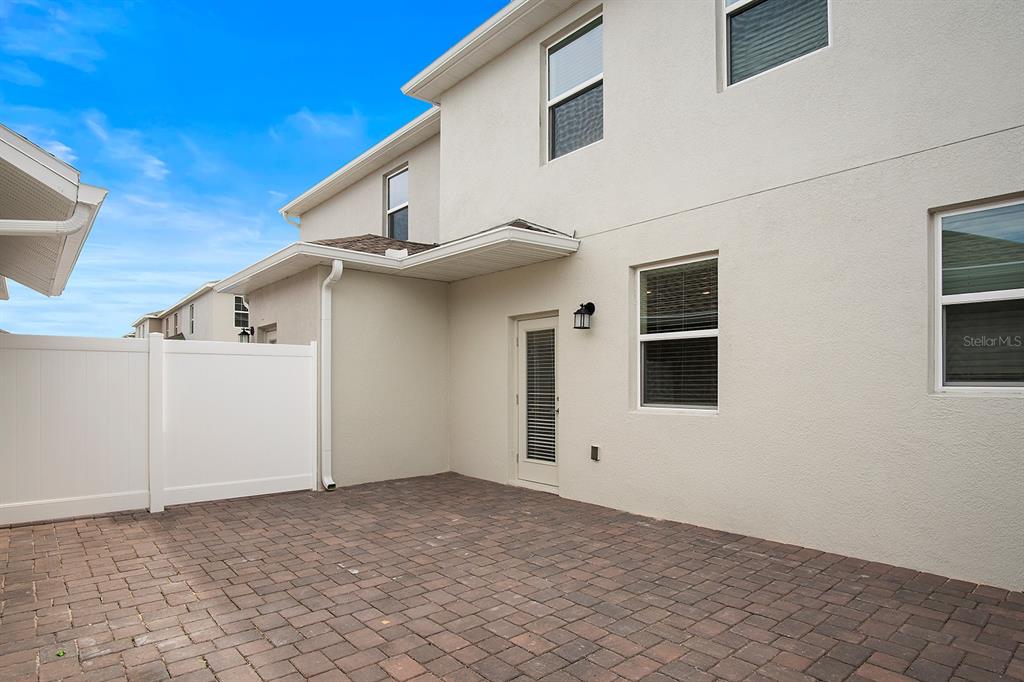A paved patio area sits beside a two-story house with a white vinyl fence — 5643 QUIET PALM LOOP, ST CLOUD, FL