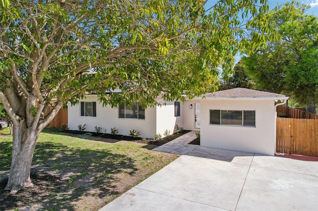 A single-story white house with a concrete driveway, a large tree, and a wooden fence — 5010 8th AVE N, ST PETERSBURG, FL