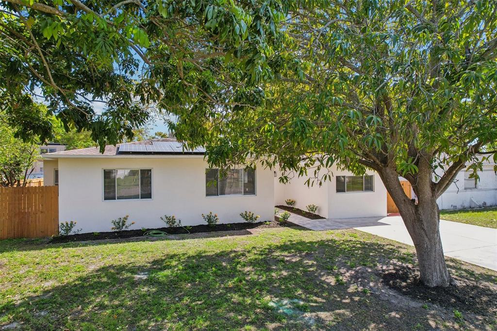 A single-story white house with solar panels and a large tree in the front yard — 5010 8th AVE N, ST PETERSBURG, FL