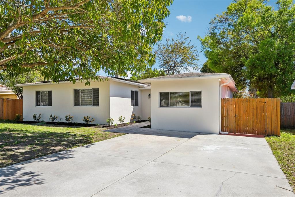 A single-story house with a concrete driveway, white stucco exterior, and a wooden fence — 5010 8th AVE N, ST PETERSBURG, FL