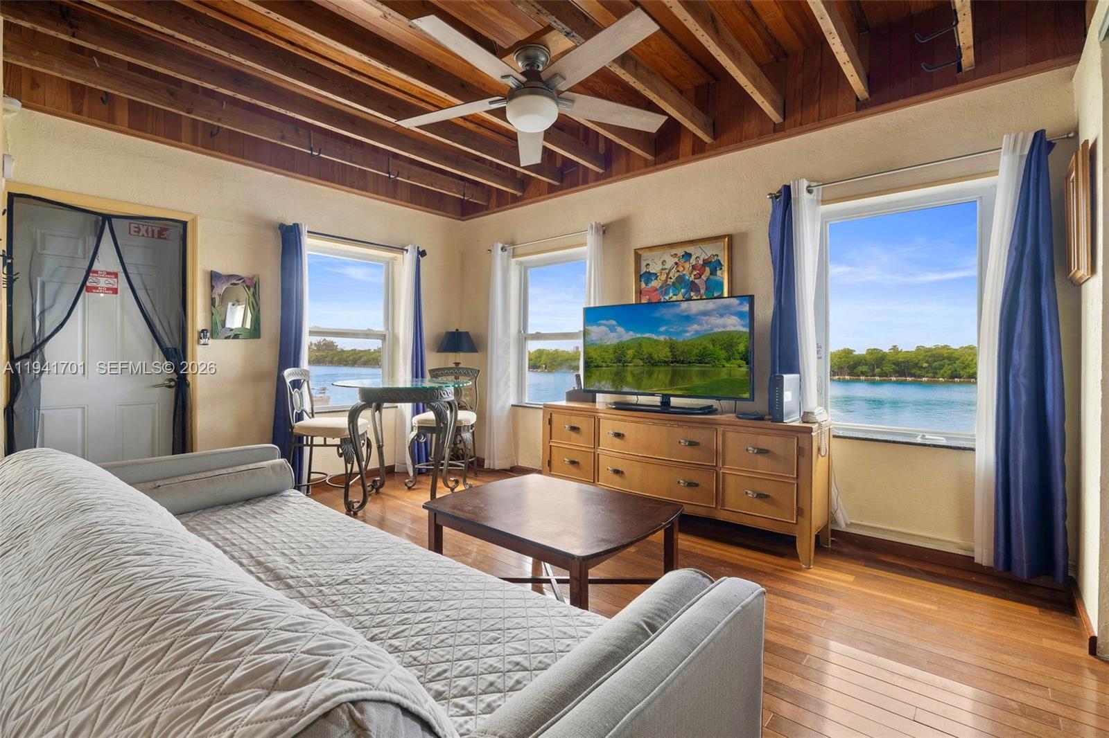 A living room features a wood-beamed ceiling, hardwood floors, and large windows overlooking the water — 1908 N Ocean Dr # 13A, Hollywood FL 33019, HOLLYWOOD, FL