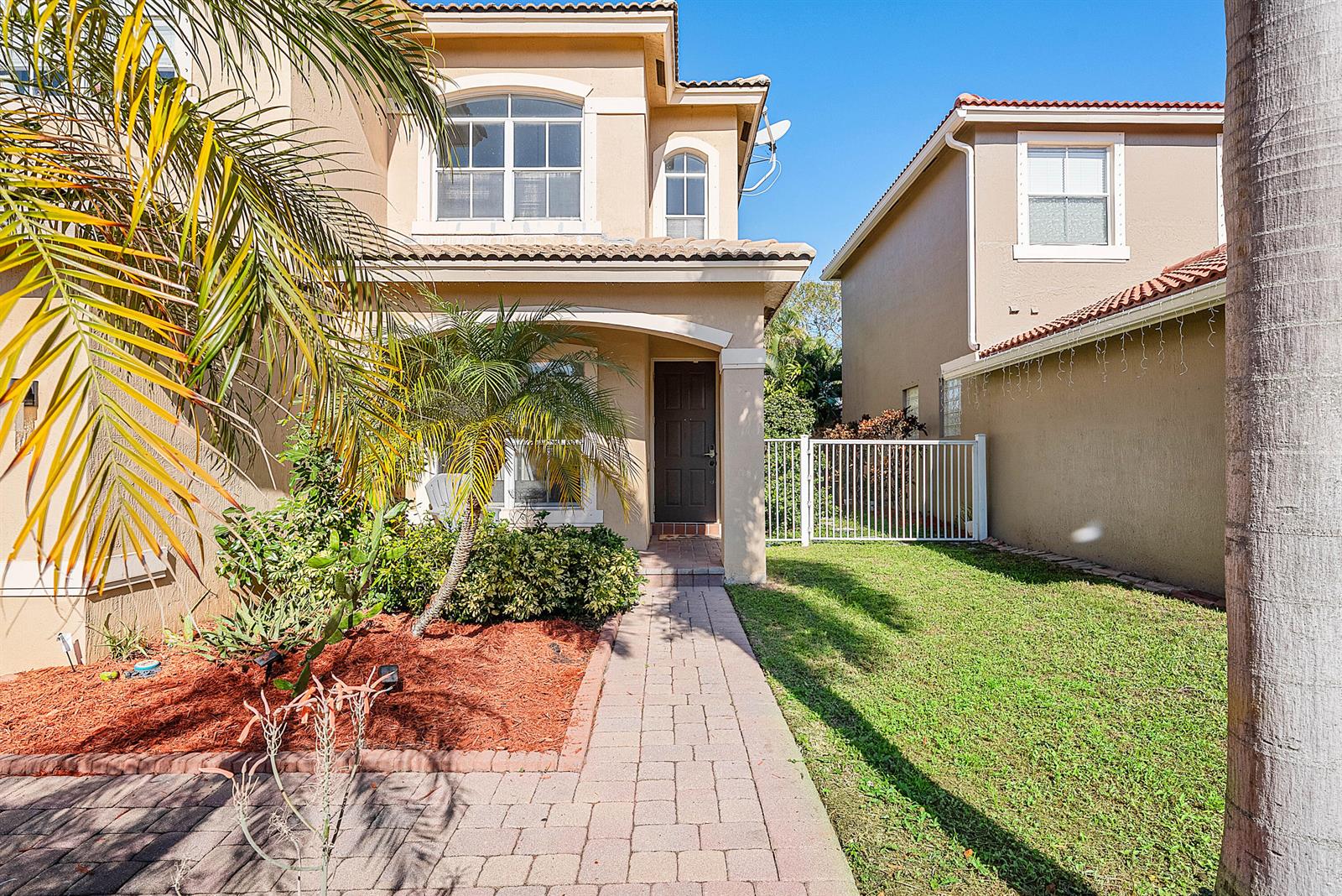 A paved walkway leads to the front entrance of a two-story tan stucco house — 5041 Massy Drive, Lake Worth FL 33463, LAKE WORTH, FL