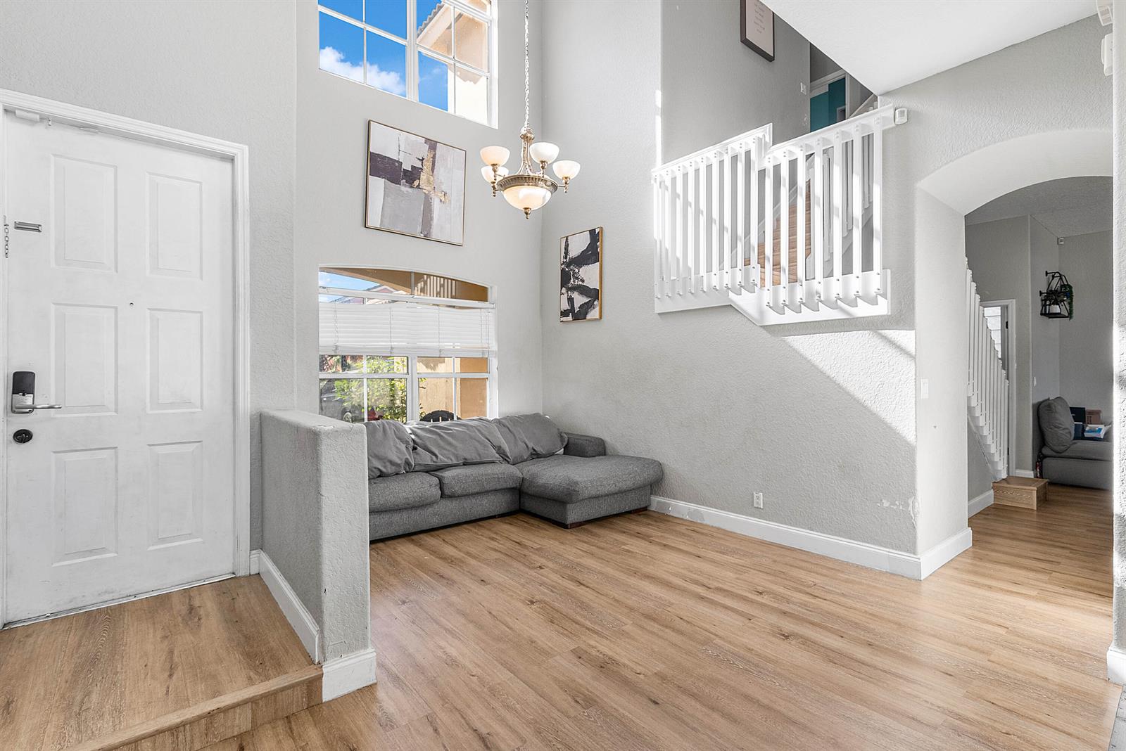 A high-ceilinged entryway features a grey sectional sofa, wood-look flooring, and a white staircase — 5041 Massy Drive, Lake Worth FL 33463, LAKE WORTH, FL