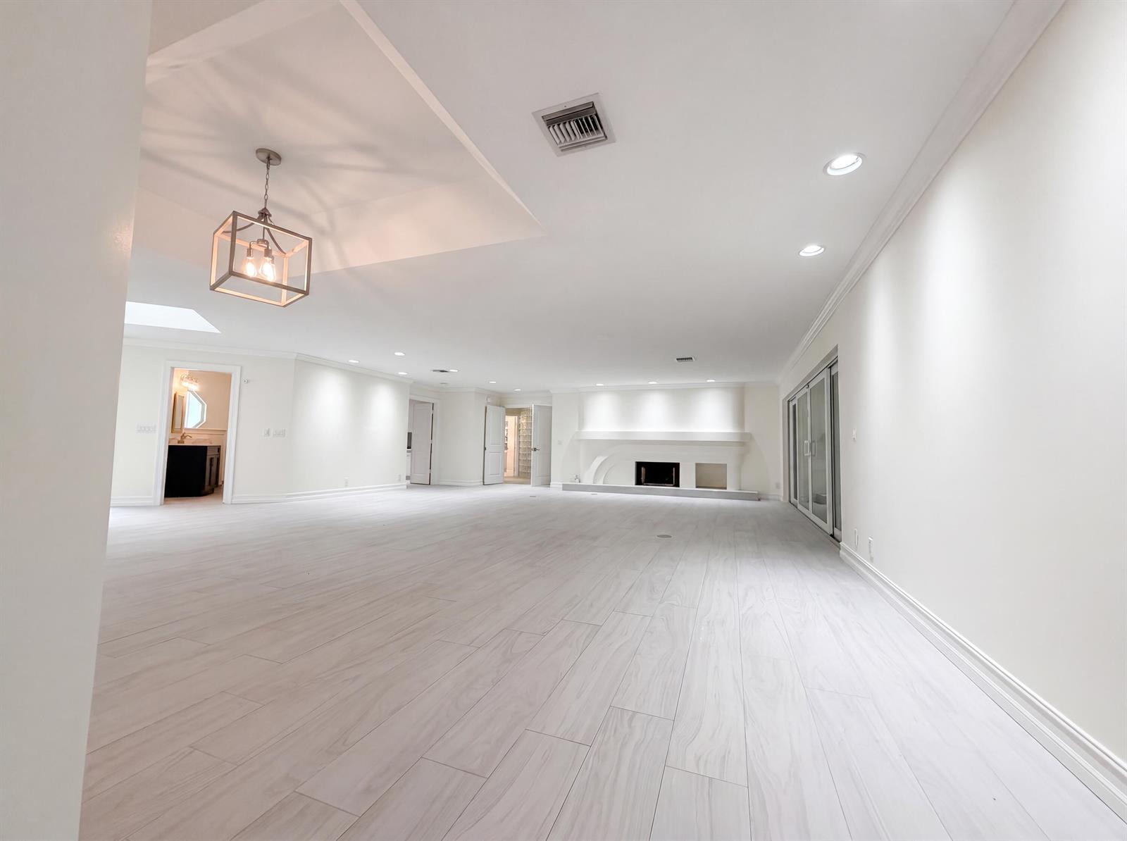 A spacious, minimalist living room features light wood-look tile flooring, recessed lighting, and a fireplace — 296 Wychmere Terrace, Wellington FL 33414, WELLINGTON, FL