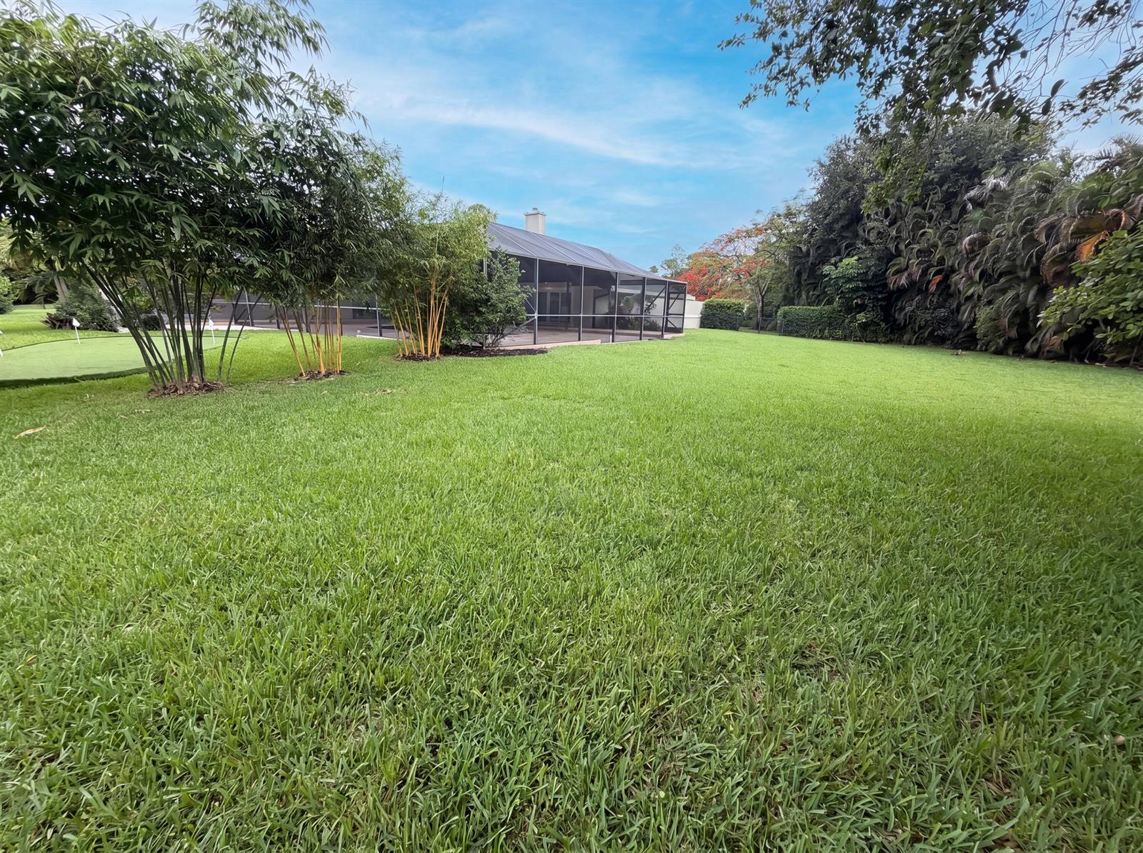 A large grassy backyard features a screened-in patio and several bamboo trees — 296 Wychmere Terrace, Wellington FL 33414, WELLINGTON, FL