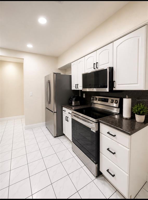 A kitchen features white cabinets, stainless steel appliances, dark countertops, and white tiled flooring — 1618 CRYSTALVIEW TRAIL, LAKELAND, FL