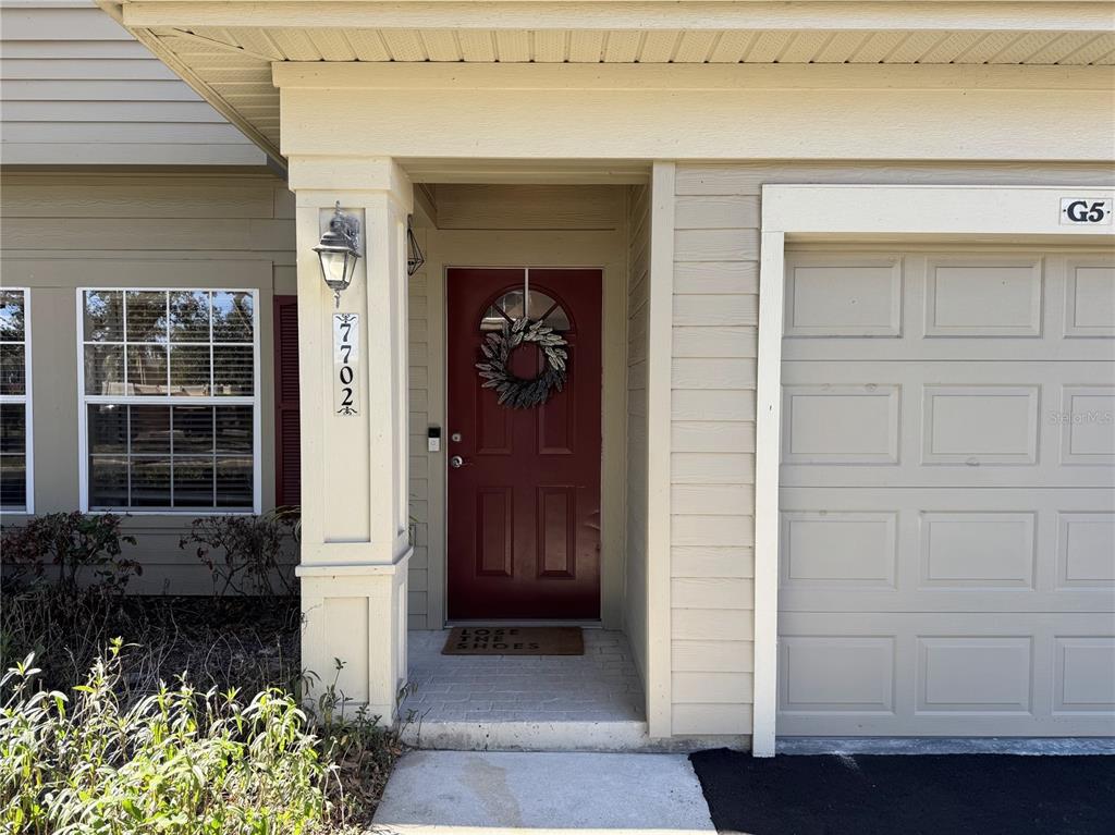 The exterior of a home features a red front door, a garage, and a house number — 7702 PLANTATION CIRCLE, BRADENTON, FL