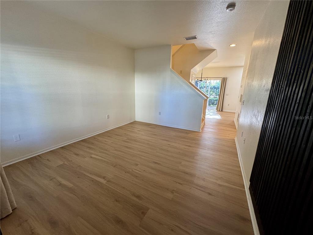 An empty room with light wood-look flooring and a staircase leading to an upper level — 7702 PLANTATION CIRCLE, BRADENTON, FL
