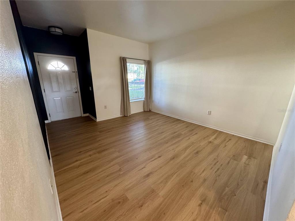 An empty room features light wood-look flooring, white walls, and a single window with curtains — 7702 PLANTATION CIRCLE, BRADENTON, FL