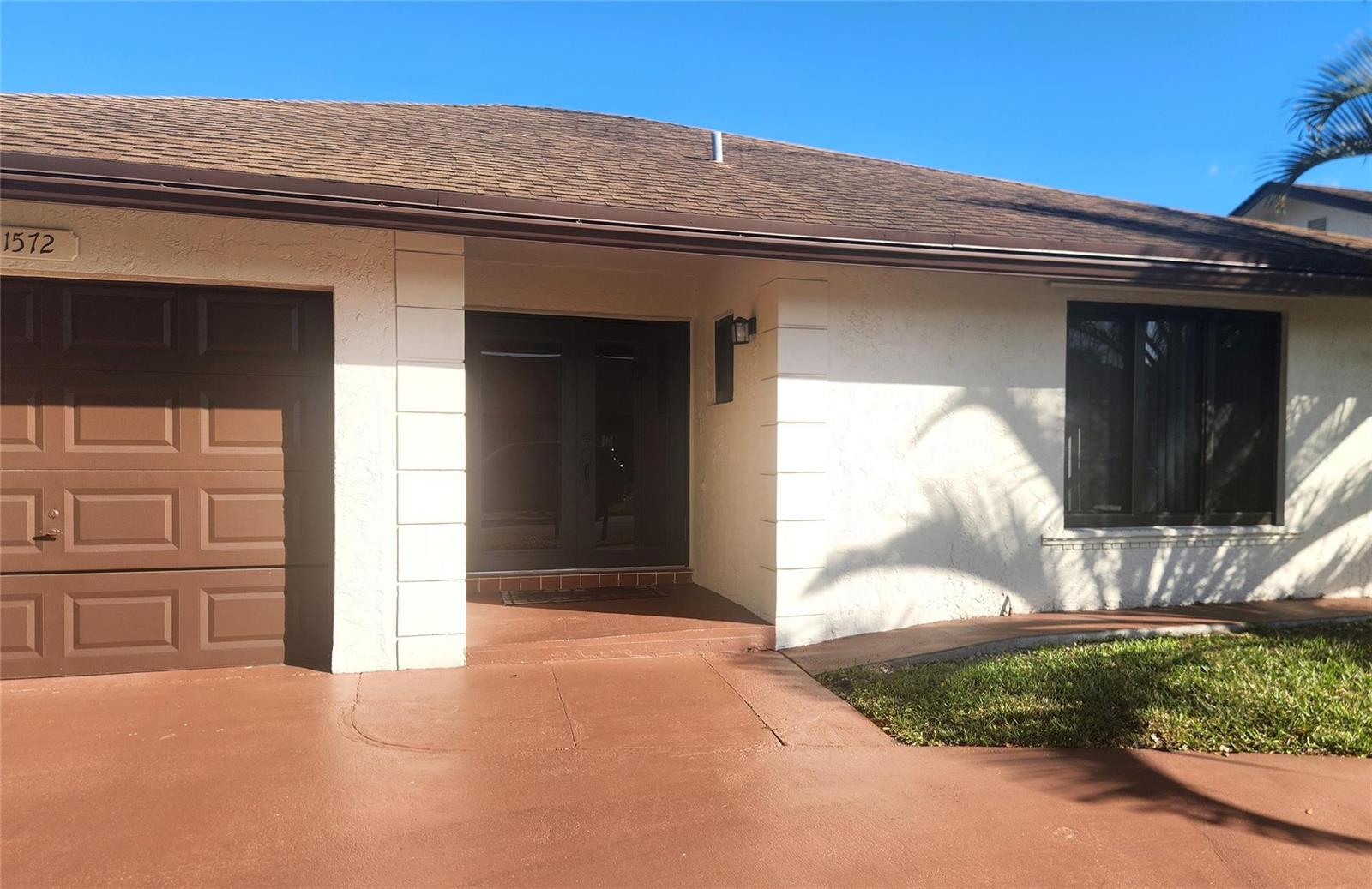 The exterior of a single-story house features a brown garage door and a front entrance — 1572 SW 23rd Terrace, Deerfield Beach FL 33442, DEERFIELD BEACH, FL