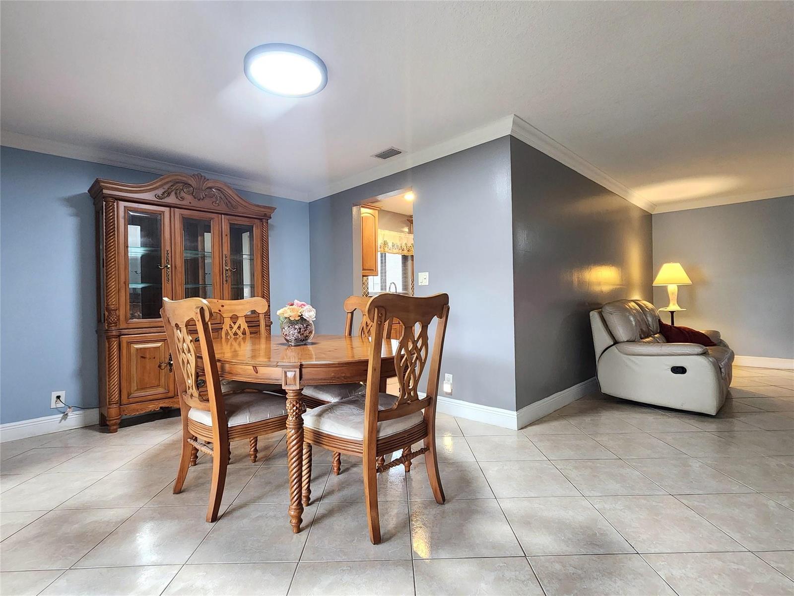 A dining area with a wooden table and hutch sits beside a living room space — 1572 SW 23rd Terrace, Deerfield Beach FL 33442, DEERFIELD BEACH, FL