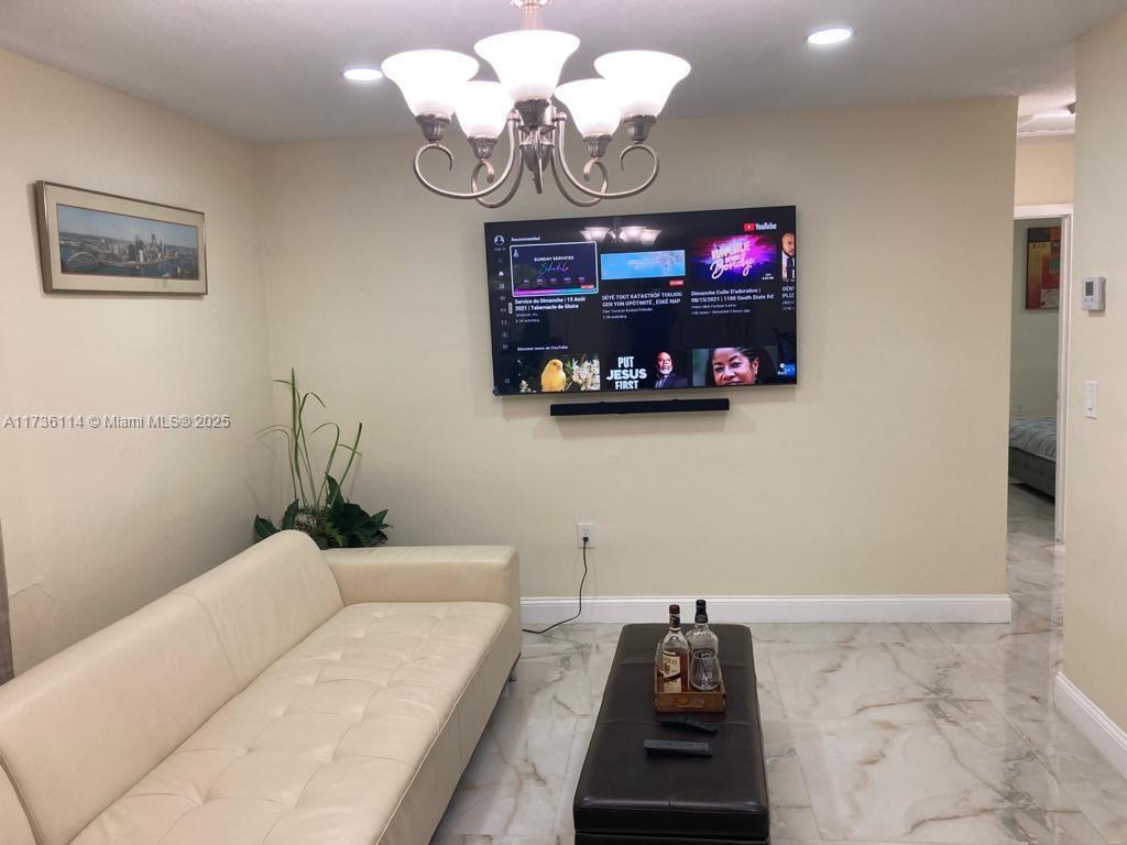 A living room features a white tufted sofa, a dark coffee table, and a wall-mounted television — 457 NE 140th St # 1, North Miami FL 33161, NORTH MIAMI, FL