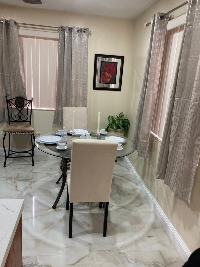 A dining area features a glass-topped table, upholstered chairs, tiled floors, and window curtains — 457 NE 140th St # 1, North Miami FL 33161, NORTH MIAMI, FL