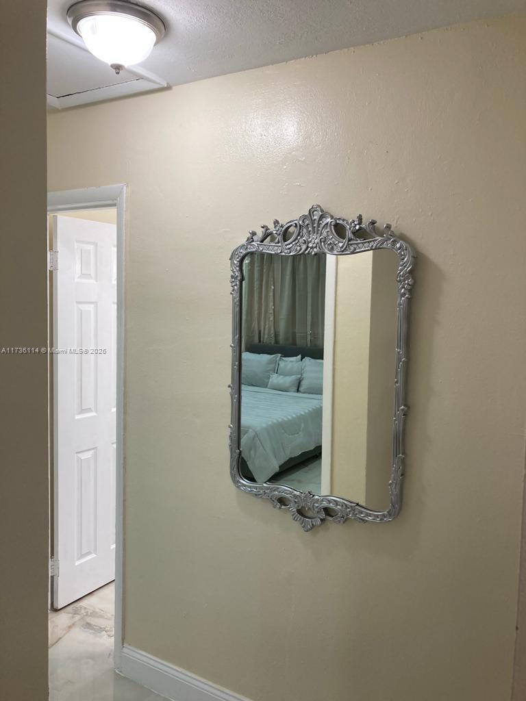 A hallway with a silver-framed mirror on a beige wall leads to a bedroom — 457 NE 140th St # 1, North Miami FL 33161, NORTH MIAMI, FL