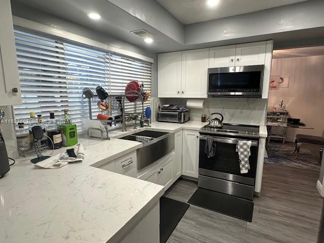 A kitchen features white cabinets, stainless steel appliances, and a farmhouse sink under a window — 6757 Arbor Dr, Miramar FL 33023, MIRAMAR, FL